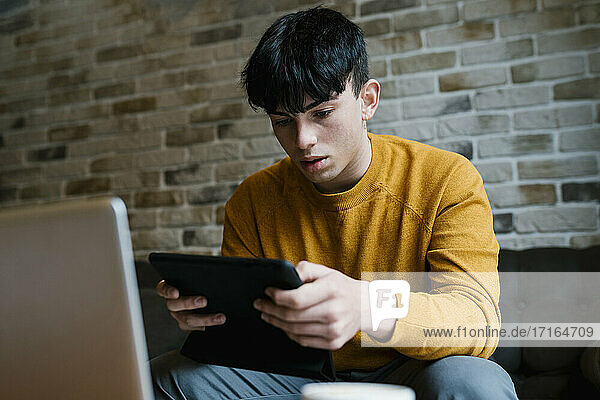 Junger Mann mit Laptop und digitalem Tablet in einem Café sitzend
