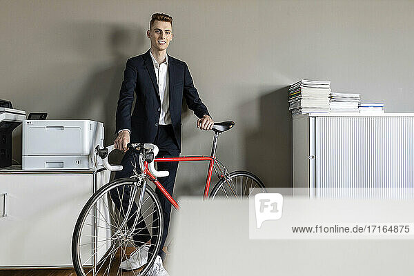 Geschäftsmann lächelt  während er mit dem Fahrrad im Büro steht