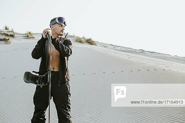 Gut aussehender junger Mann mit Sandbrett  der in der Wüste von Almeria  Tabernas  Spanien  steht und träumt