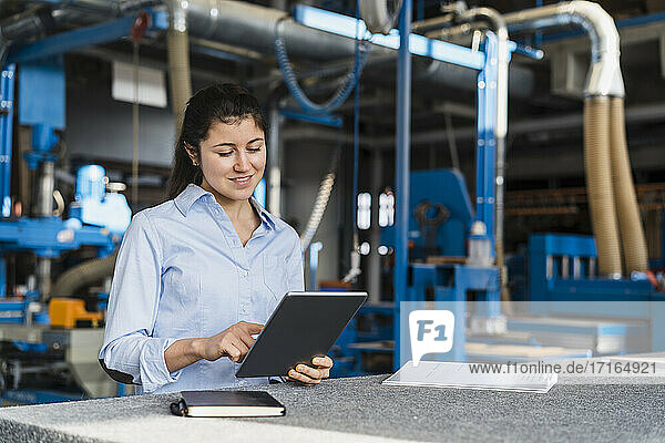 Smiling expertise using digital tablet while standing at industry