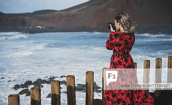 Junge Frau  die durch eine Kamera fotografiert  während sie in El Golfo  Lanzarote  Spanien steht