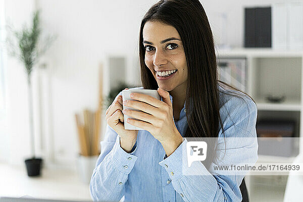 Lächelnde Geschäftsfrau  die im Büro sitzend Kaffee trinkt