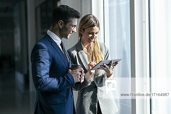 Geschäftsfrau  die lächelnd ein digitales Tablet benutzt  das neben einem Kollegen im Büro steht
