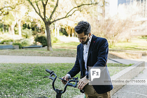 Businessman using mobile phone while standing by bicycle at park