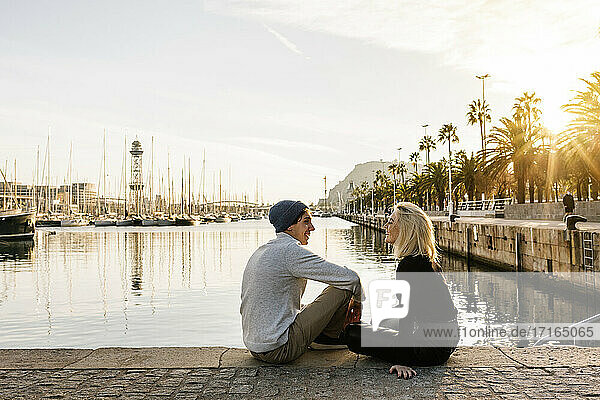 Young man with girlfriend sitting at harbor against sky