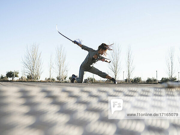 Junge Frau mit Schwert übt Kampfsport im Park gegen klaren Himmel