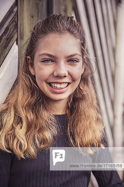 Smiling girl staring while standing against barn door