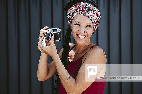 Lächelnde Frau stellt das Kameraobjektiv ein  während sie an der Wand steht