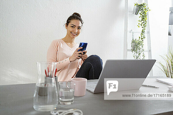 Smiling woman using mobile phone while sitting at home office