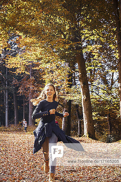 Smiling girl running in forest during autumn