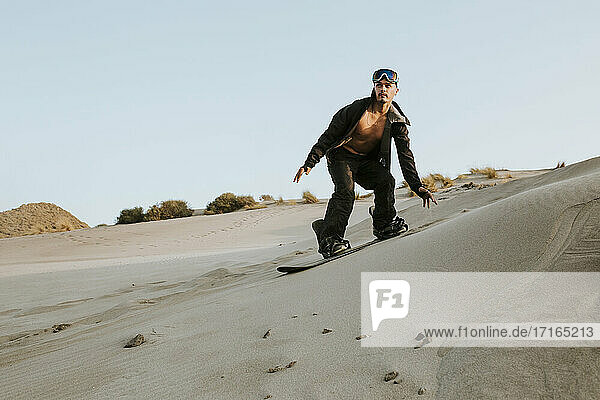 Young man looking away while sandboarding against clear sky at Almeria  Tabernas desert  Spain