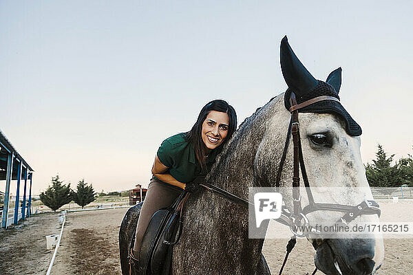 Lächelnde Frau auf einem Pferd sitzend gegen den klaren Himmel auf einem Bauernhof