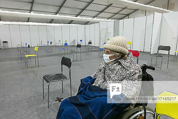 Ältere Frauen mit Schutzmaske und warmer Kleidung sitzen im Rollstuhl im Impfzentrum
