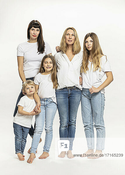 Confident mothers and daughters standing against white background in studio