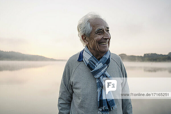 Smiling man wearing scarf looking away while standing against lake