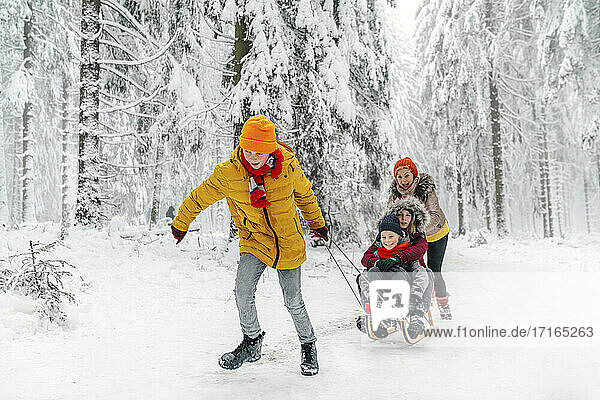 Familie spielt beim Schlittenfahren auf Schnee im Wald