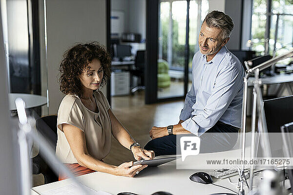 Businesswoman showing digital tablet to colleague while working at open plan office