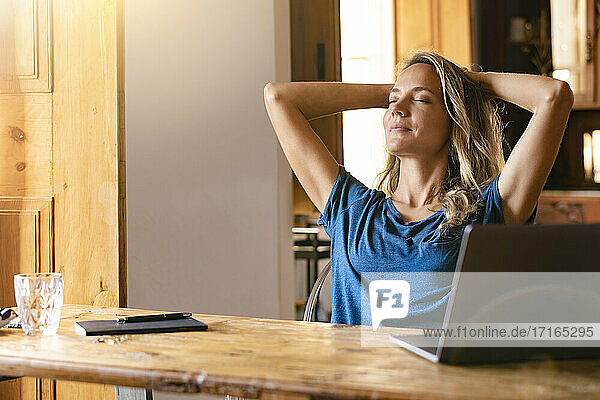 Female freelancer with hands behind head relaxing in living room