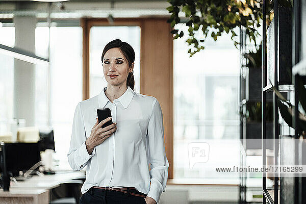 Geschäftsfrau mit Mobiltelefon im Büro stehend