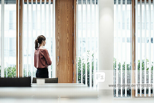 Geschäftsfrau schaut durch ein Fenster  während sie im Büro steht