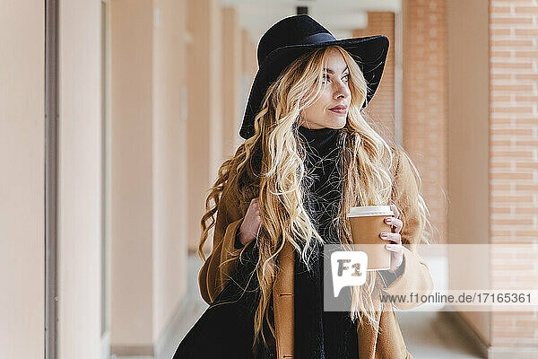 Woman in hat holding coffee cup while looking away