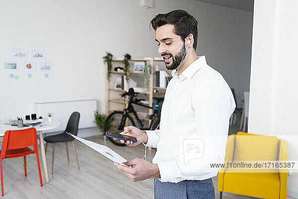 Junger Geschäftsmann mit Papierdokumenten  die er bei einem Telefongespräch im Büro bespricht
