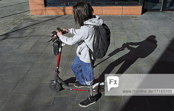 Young disabled man using smart phone while standing on electric push scooter during sunny day
