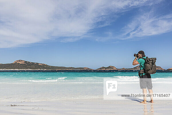 Mann mit Rucksack beim Fotografieren der türkisfarbenen Bucht  Westaustralien