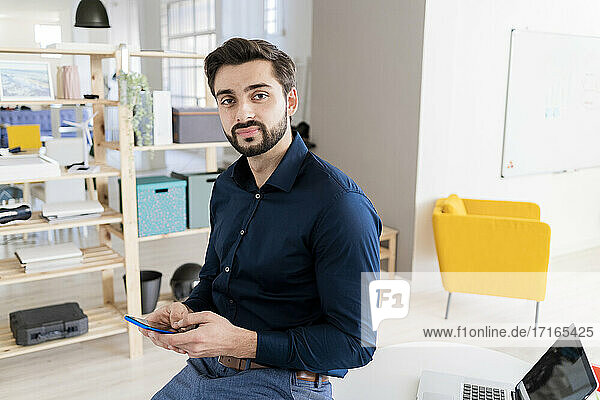 Young businessman sitting at desk while using smart phone in office