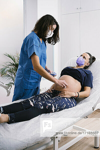 Midwife in protective face mask examining pregnant woman during COVID-19