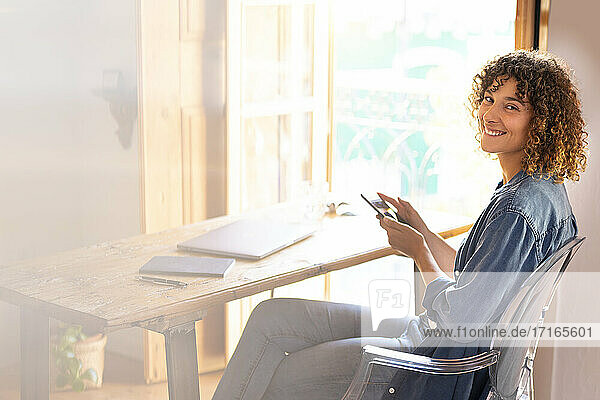 Happy female freelancer with mobile phone sitting at home office