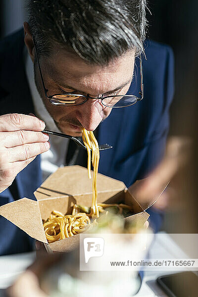 Businessman eating noodles while sitting in cafeteria at office