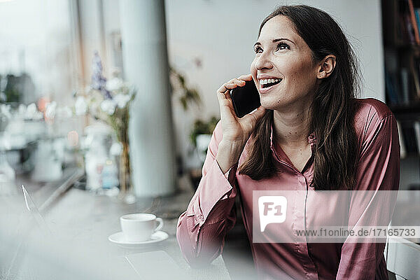 Lächelnde Unternehmerin  die mit ihrem Smartphone spricht und im Café nach oben schaut