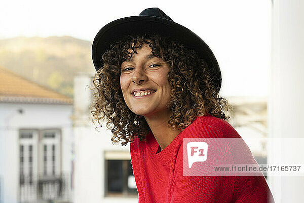 Curly woman wearing hat in balcony