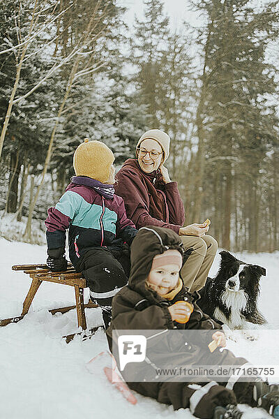 Family with Border Collie sitting on sled at snow covered field during weekend