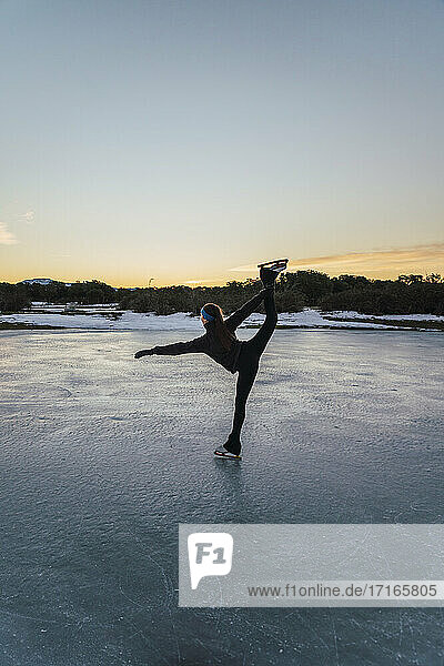 Female figure skater practicing on frozen lake at dusk