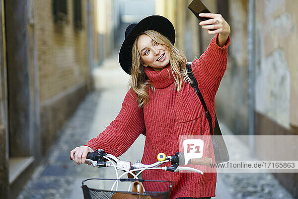 Smiling woman taking selfie through mobile phone while standing with bicycle on footpath