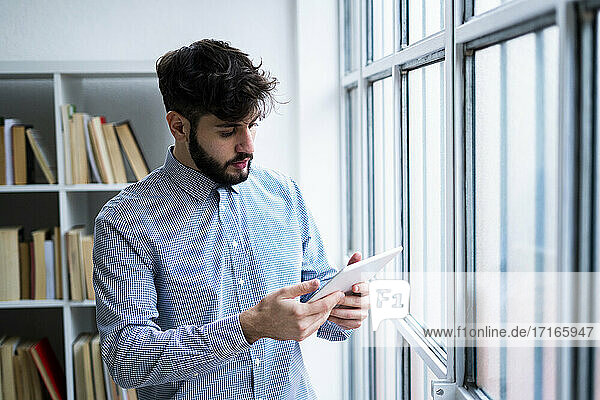 Junger Geschäftsmann benutzt digitales Tablet am Fenster in einem kreativen Büro