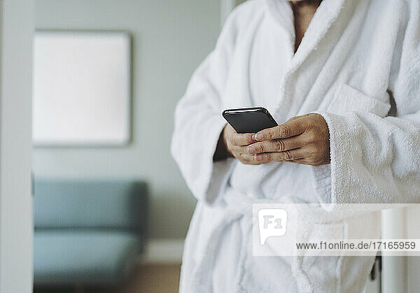 Man wearing bathrobe using smart phone in hotel room