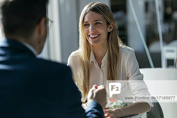 Smiling businesswoman having lunch with colleague while sitting in cafeteria at office