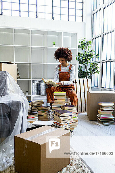 Afro-Frau packt Bücher aus  während sie an einem Regal in ihrer neuen Loft-Wohnung sitzt