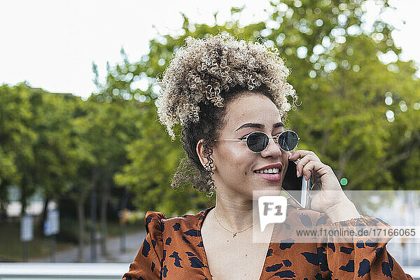 Lächelnde Frau  die wegschaut  während sie mit einem Handy in der Stadt telefoniert
