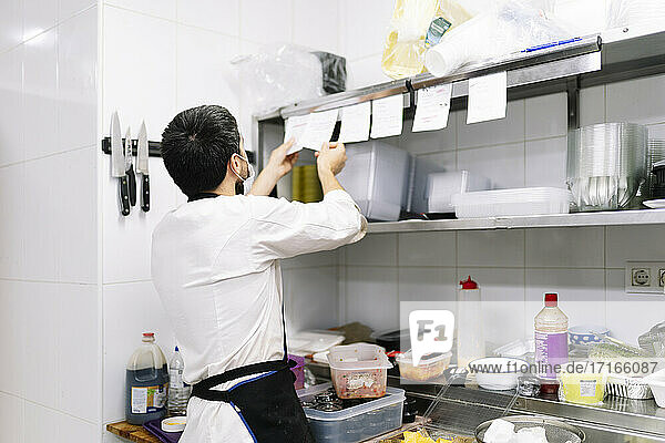 Junger männlicher Koch  der bei der Arbeit in der Küche eines Restaurants die Bestellungen überprüft