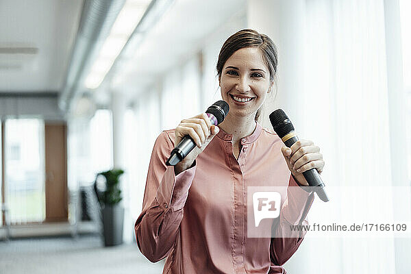Lächelnde Geschäftsfrau  die im Büro durch ein Mikrofon singt