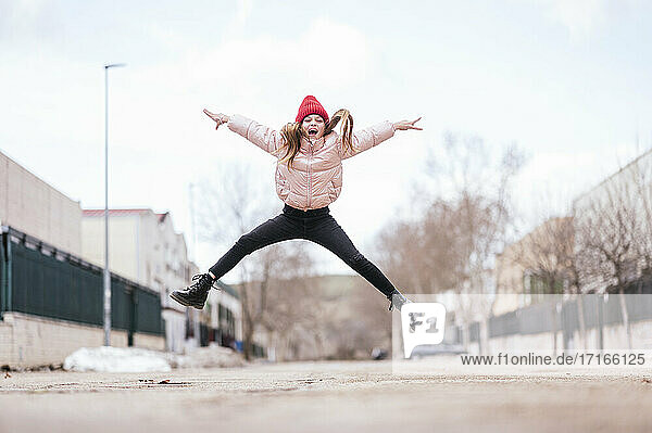Cheerful girl jumping on road against sky