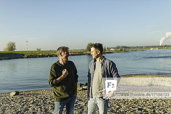 Cheerful father and son discussing while standing against river on sunny day