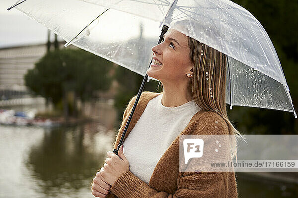Happy woman looking up while holding umbrella during rainy season