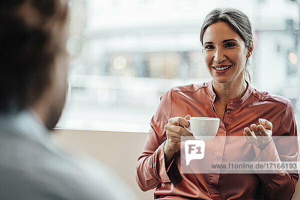 Smiling businesswoman having coffee while discussing with male colleague at cafe