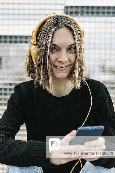 Portrait of smiling young woman listening to music outdoors