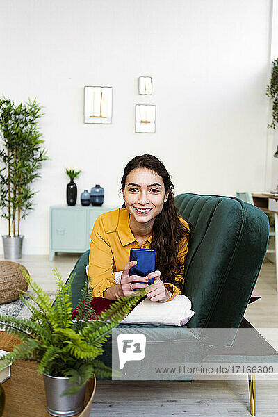Smiling woman using mobile phone while lying on sofa at home